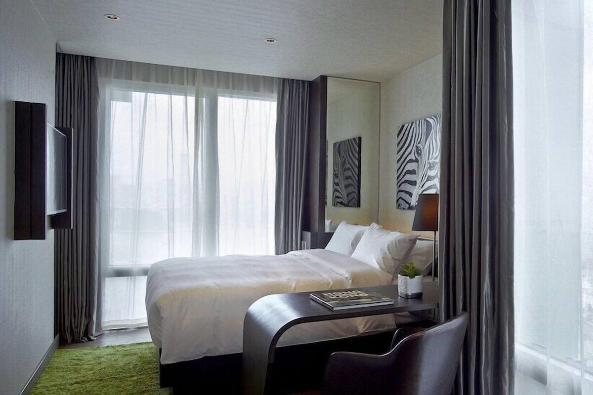 A hotel room with a large bed, a desk with a chair, a TV, and a window with curtains.