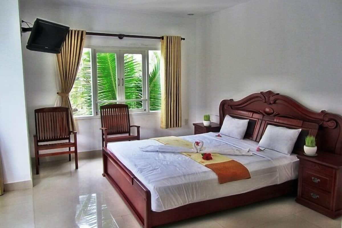 A neatly arranged hotel room with a large bed, a wooden chair, a TV mounted on the wall, and a window with curtains.