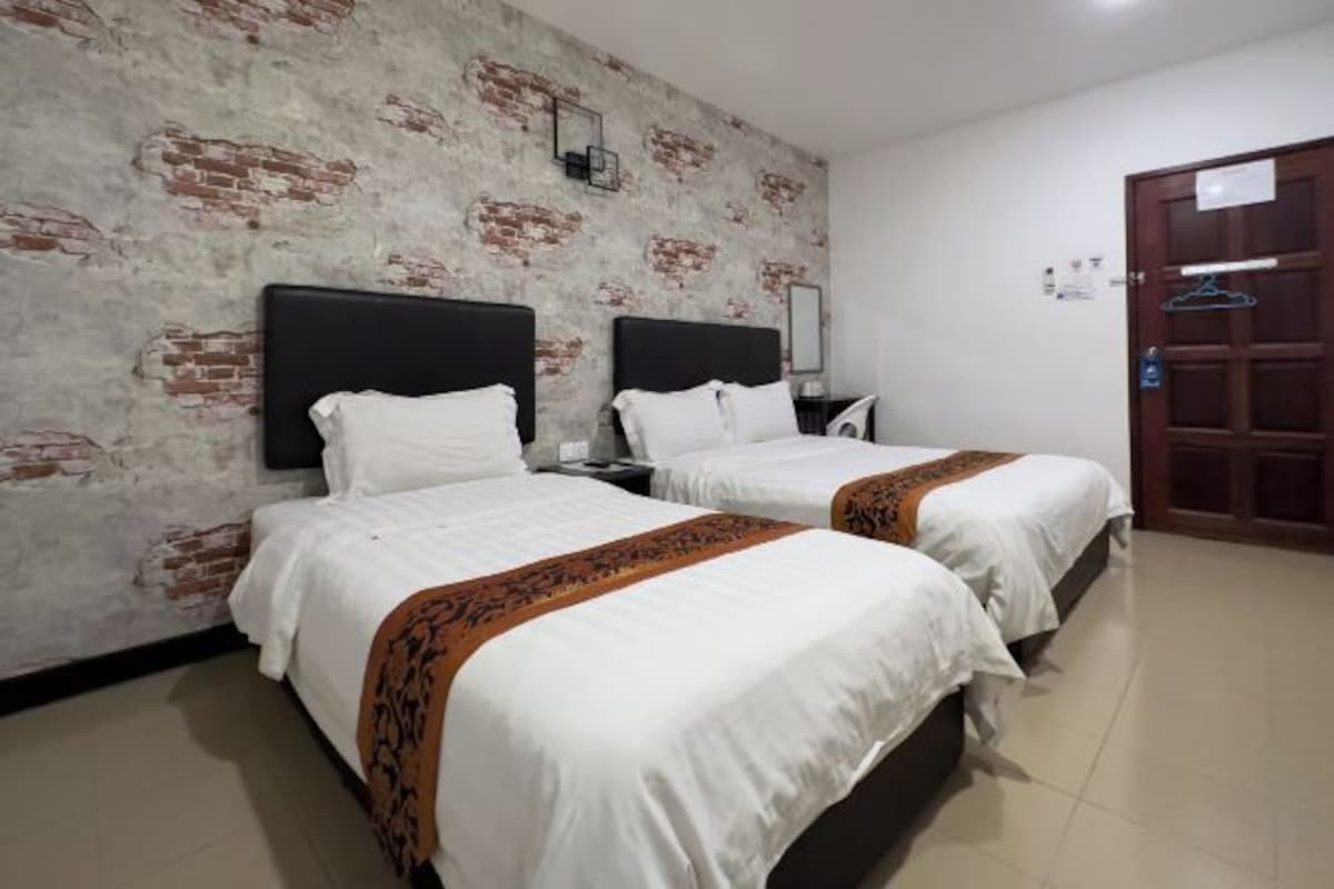 Habitación de hotel con dos camas, una pared de ladrillo, una puerta de madera y un pequeño escritorio con espejo.