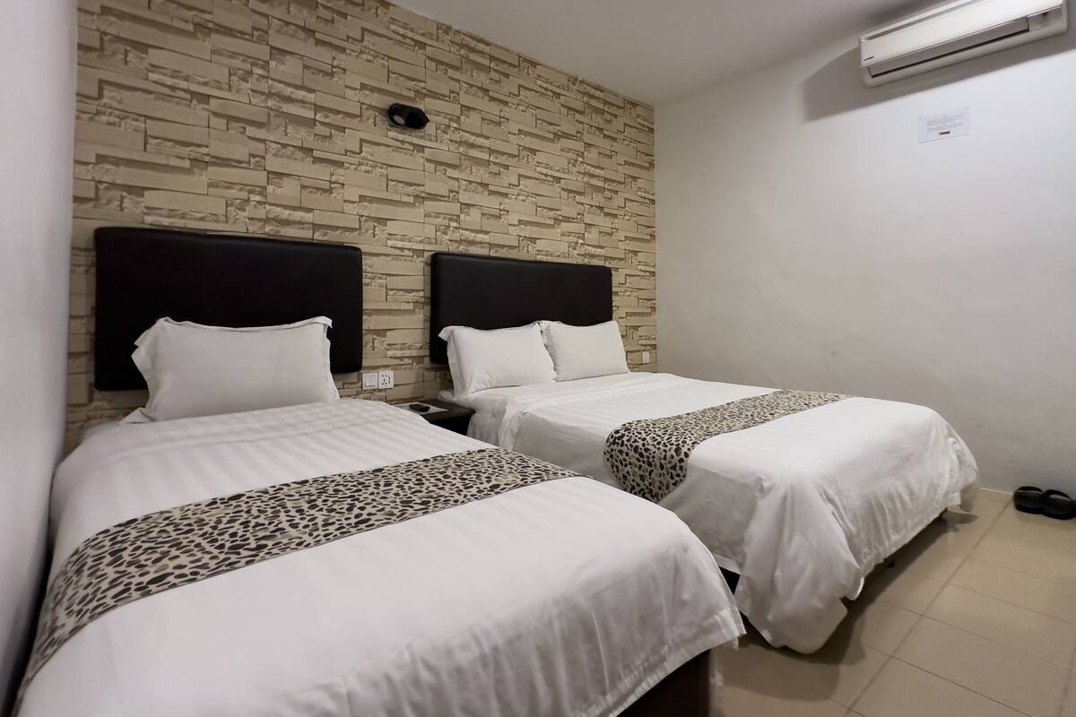 A hotel room with two beds, a stone-patterned wall, and a ceiling-mounted air conditioning unit.
