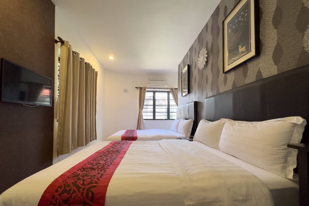 A hotel room with two beds, a TV, and a window with curtains.
