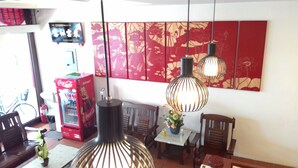 Uma área de refeições com uma geladeira vermelha Coca-Cola, duas luminárias pendentes e uma parede com padrão floral.