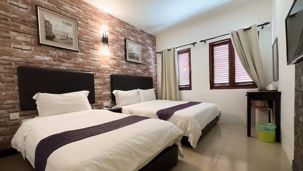 Quarto de hotel com duas camas, parede de tijolos e quadros emoldurados.