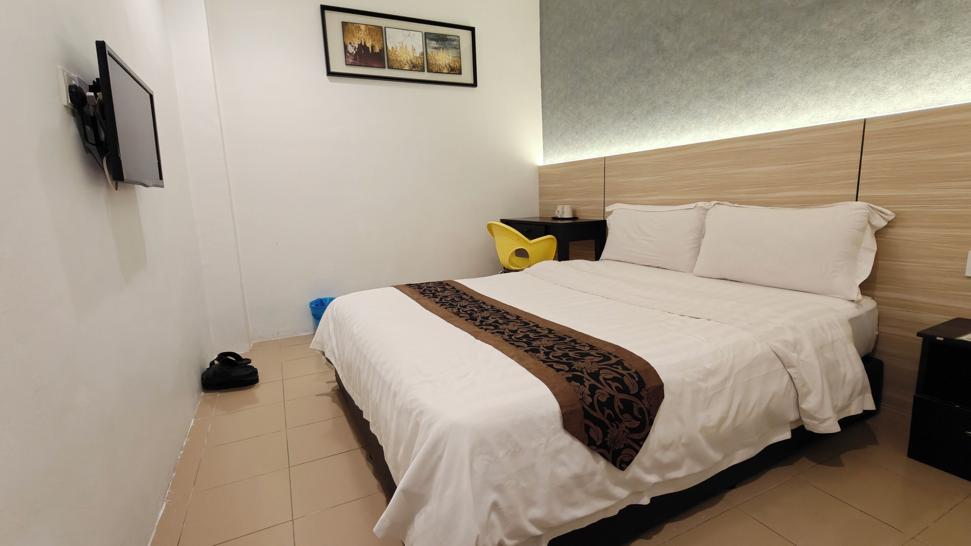 Une chambre d’hôtel équipée d’un lit, d’un bureau, d’une chaise et d’un téléviseur fixé au mur.
