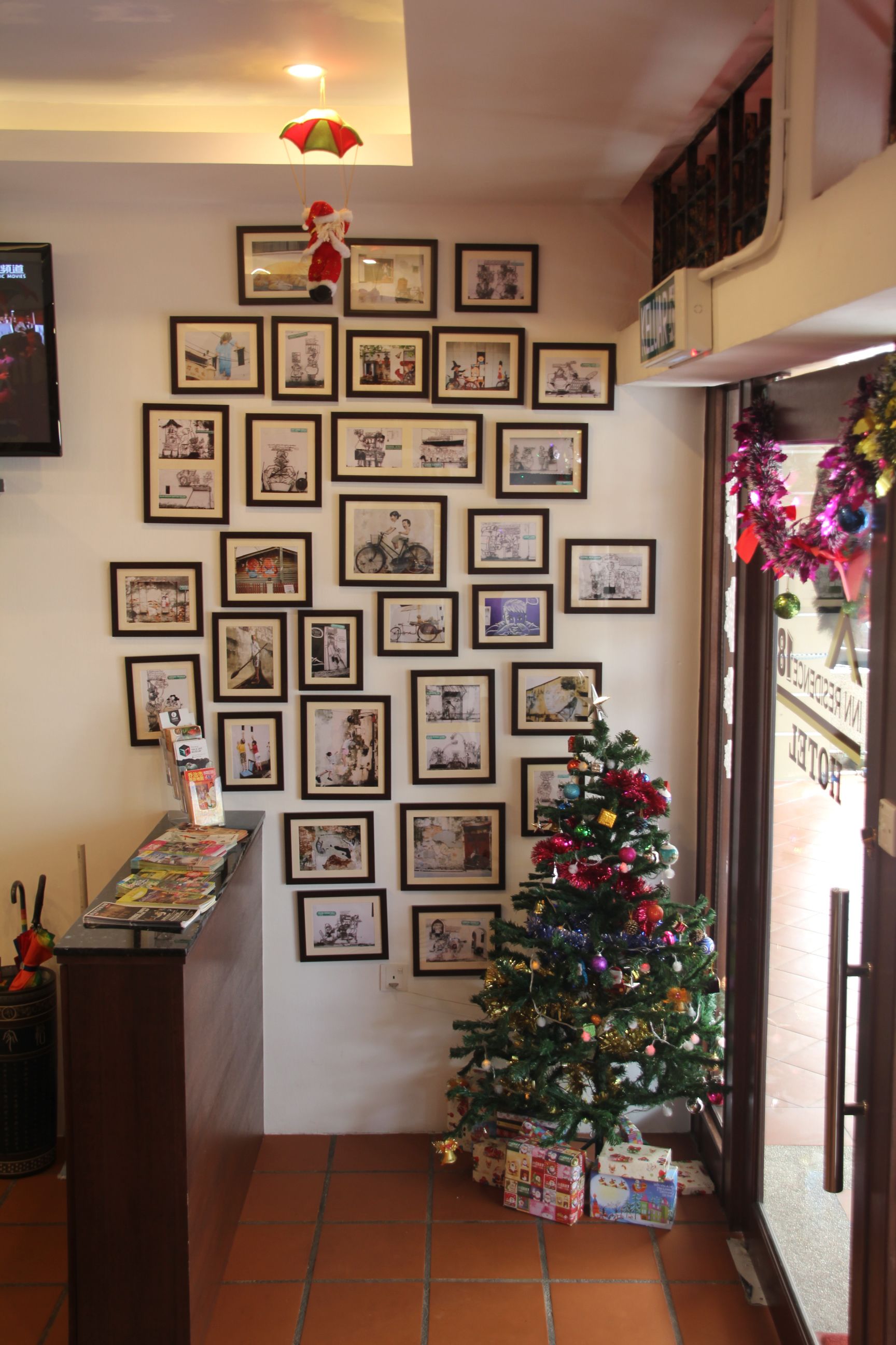 Une pièce dont un mur est décoré de tableaux encadrés, avec un petit sapin de Noël et quelques cadeaux.