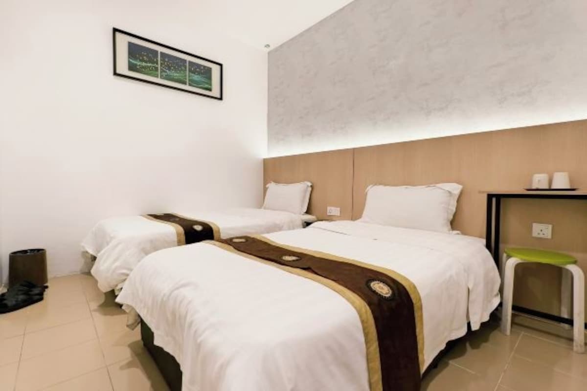 Habitación de hotel con dos camas, una mesita de noche, una silla y una estantería en la pared.