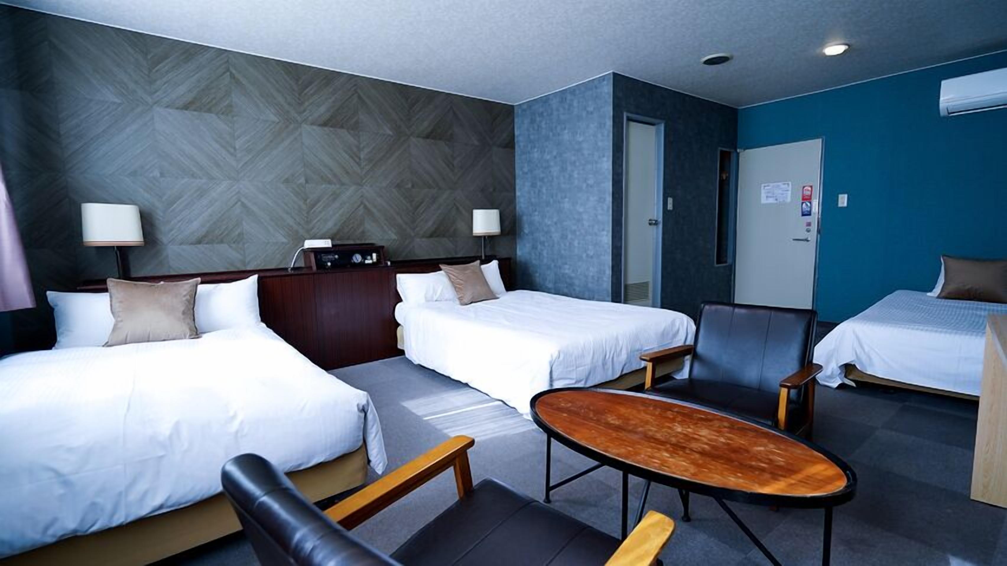 A hotel room with two beds, a desk, a chair, and a small table.