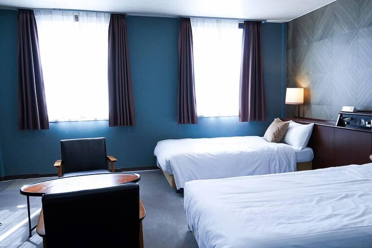 Ein Hotelzimmer mit zwei Betten, einem Schreibtisch, einem Stuhl, einem Nachttisch und einer Lampe.