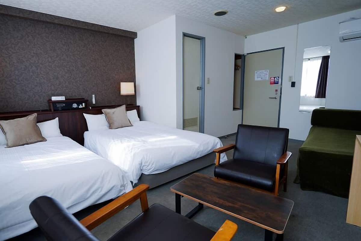 Ein Hotelzimmer mit zwei Betten, einem Schreibtisch, einem Sessel, einer Couch und einem an der Wand befestigten Fernseher.