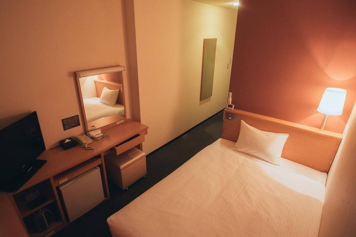 Ein Hotelzimmer mit einem Bett, einem Schreibtisch mit Telefon, einem Spiegel und einem Nachttisch mit Lampe.