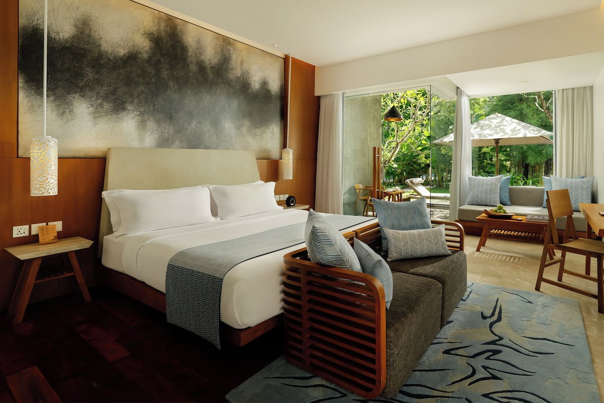 A hotel room with a large bed, a sofa, a dining table, and a view of the outdoors.