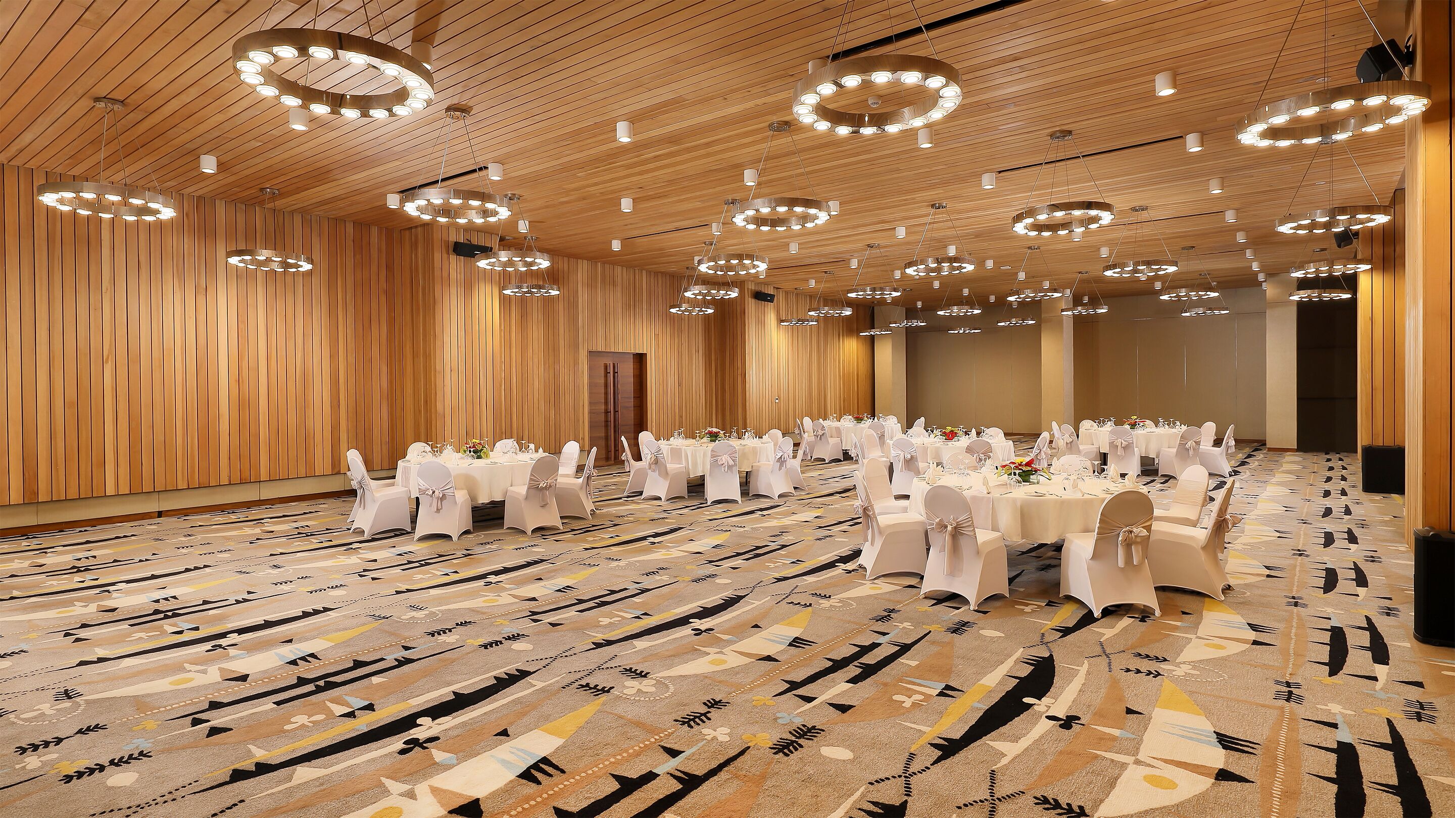 A banquet hall with round tables set for events, wooden panel walls, and a patterned carpet.