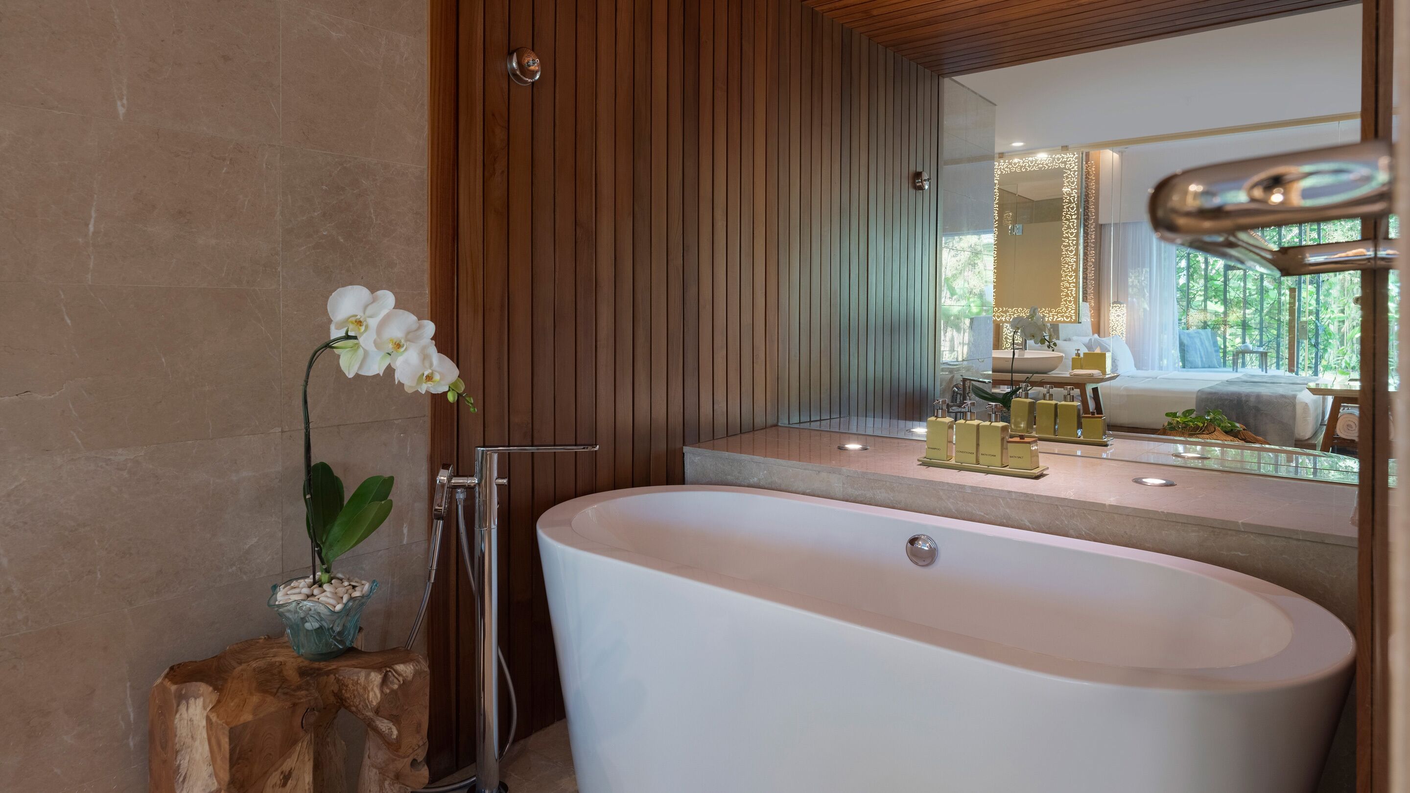 A modern bathroom with a freestanding bathtub, a wooden panel wall, a large mirror, and a potted orchid.