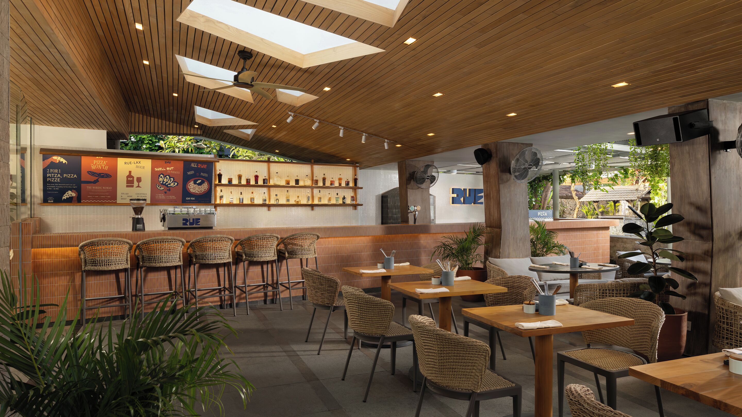 A restaurant with wooden ceiling, bar area, and seating with wicker chairs and tables.