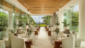 A modern interior with glass walls, white furniture, and a view of a green landscape. - Maya Sanur Resort & Spa (Denpasar)