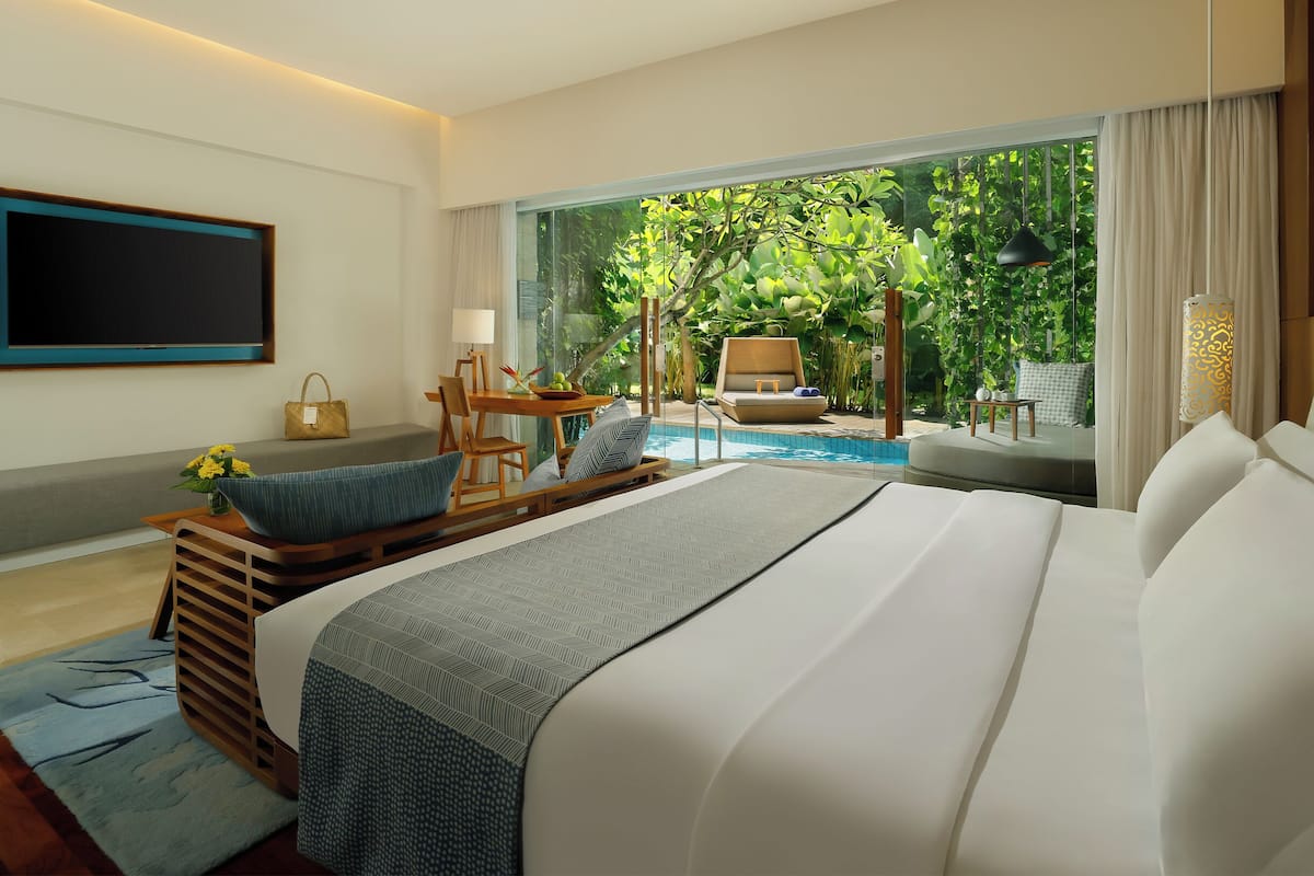 A modern hotel room with a large bed, a TV, a pool view, and a dining area.