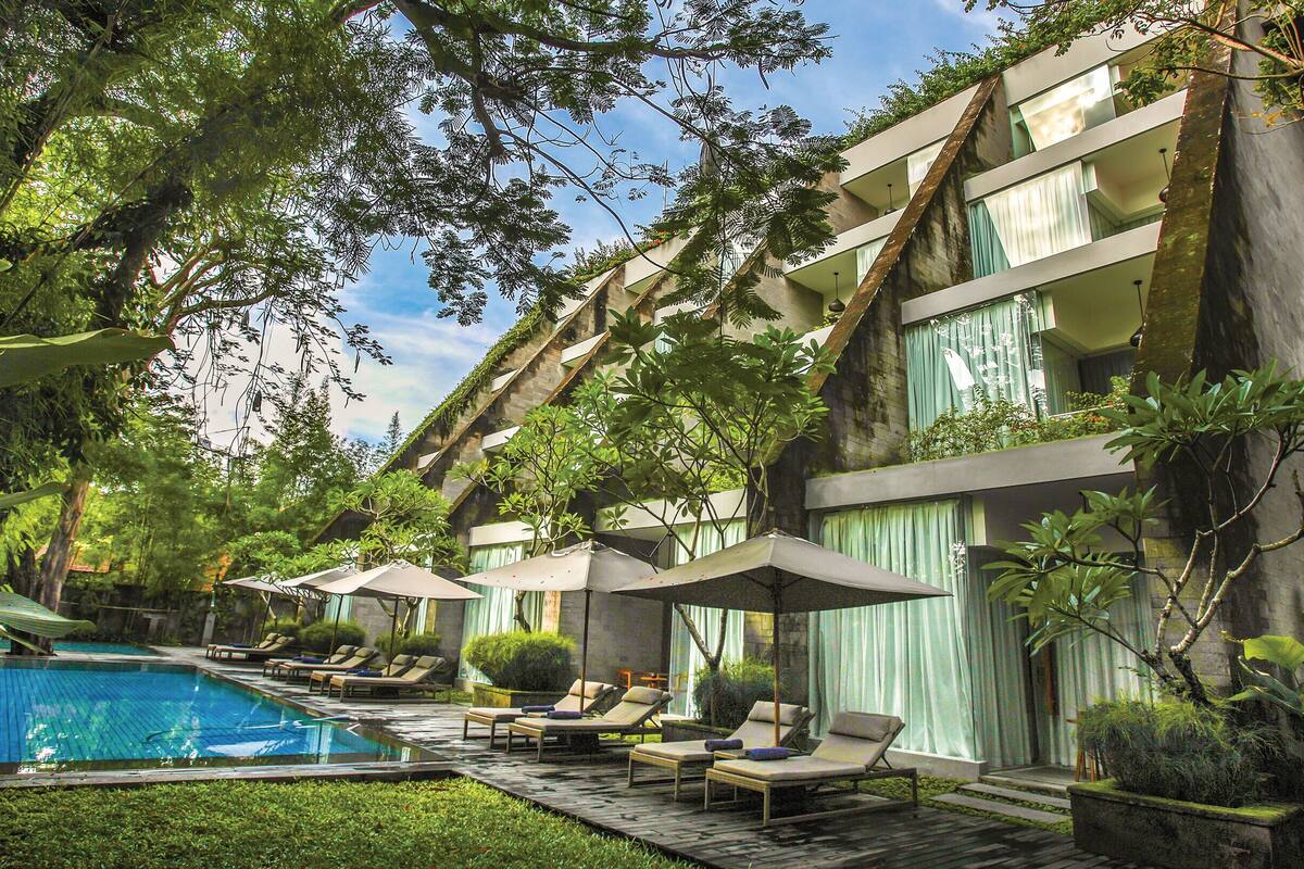 A hotel with a swimming pool, lounge chairs, and umbrellas.