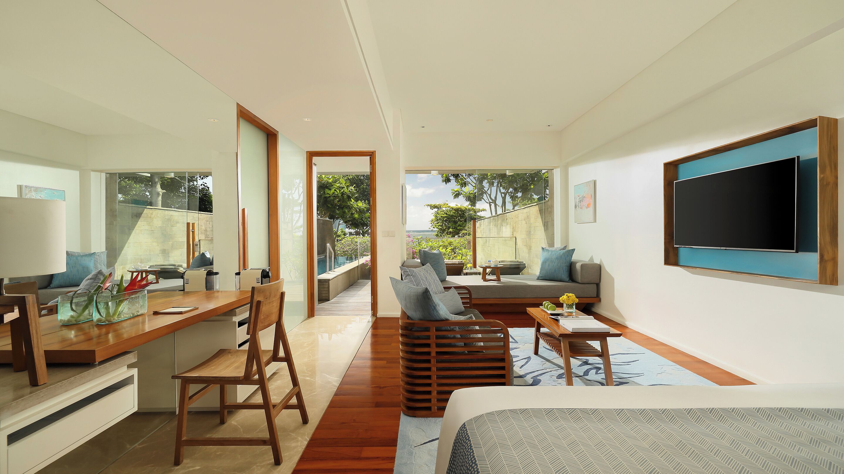 Habitación de hotel moderna con un escritorio de madera, un sofá, un televisor y vistas al exterior.