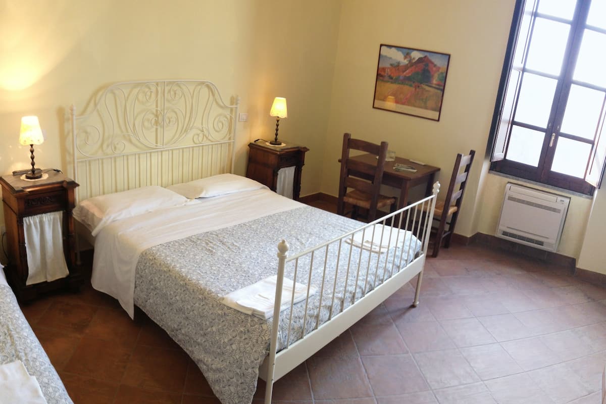 Une chambre à coucher avec un lit, deux tables de chevet avec des lampes, une chaise, une table et un radiateur.