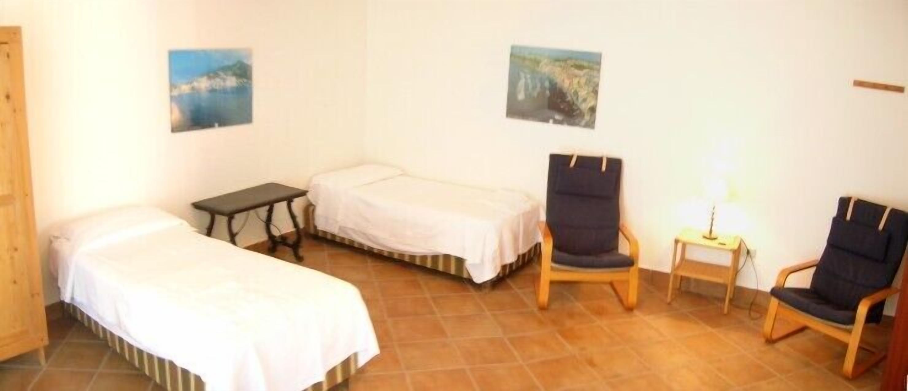 A small room with two single beds, a chair, and a table.