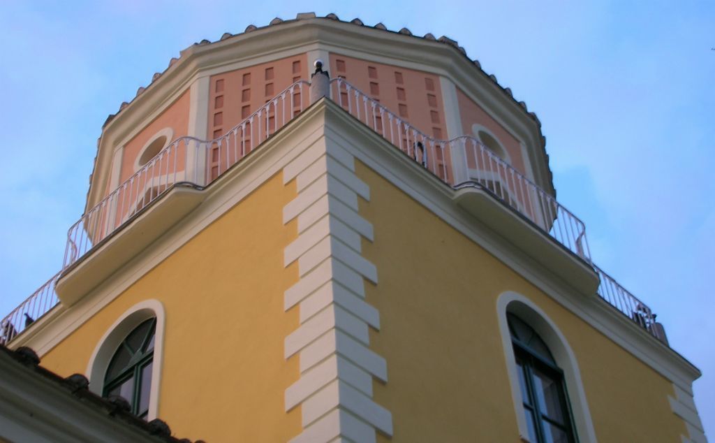 A building with a yellow facade and a pink upper section, featuring a balcony with white railings.