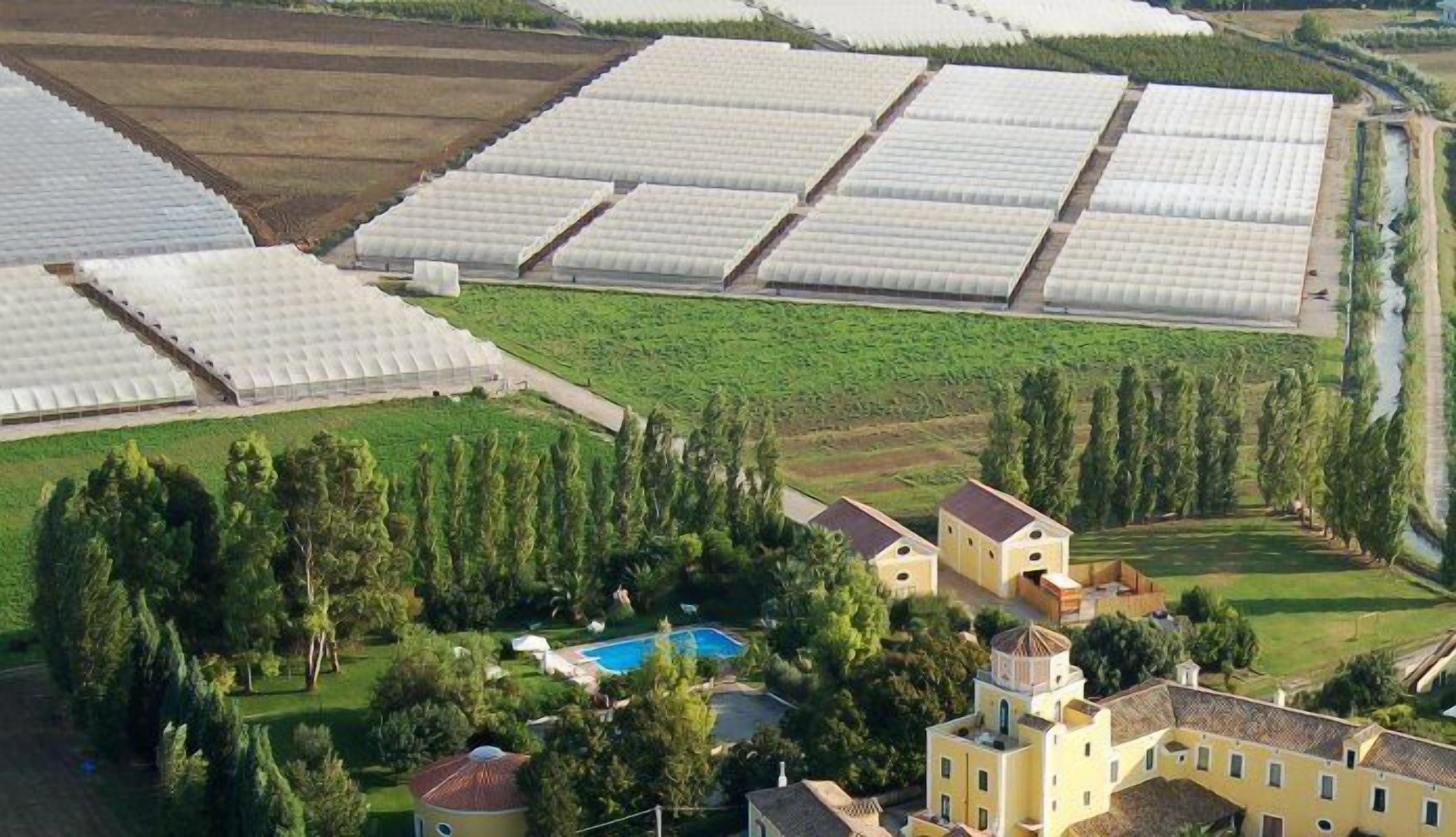 Vue aérienne d’un vaste complexe agricole doté de nombreuses serres, entouré d’arbres et comprenant une piscine.