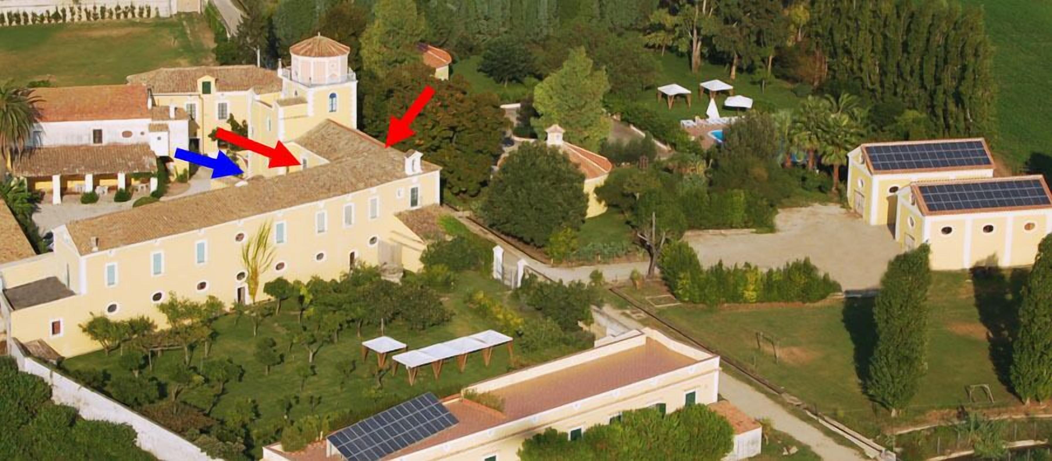 An aerial view of a property with multiple buildings, including a large central building with a dome, smaller structures, and solar panels.