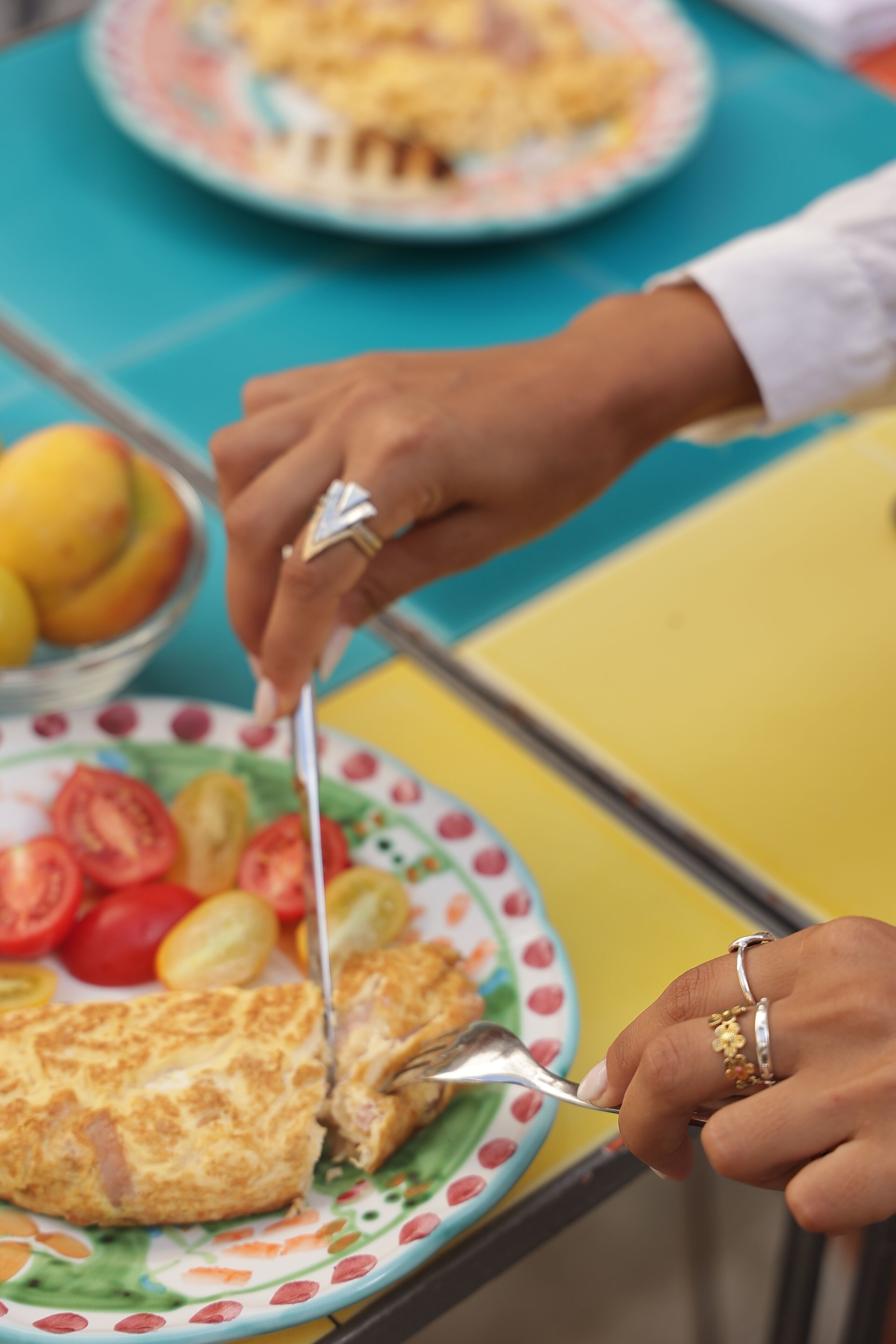 A person cutting a slice of omelette on a plate with tomatoes and lemons.