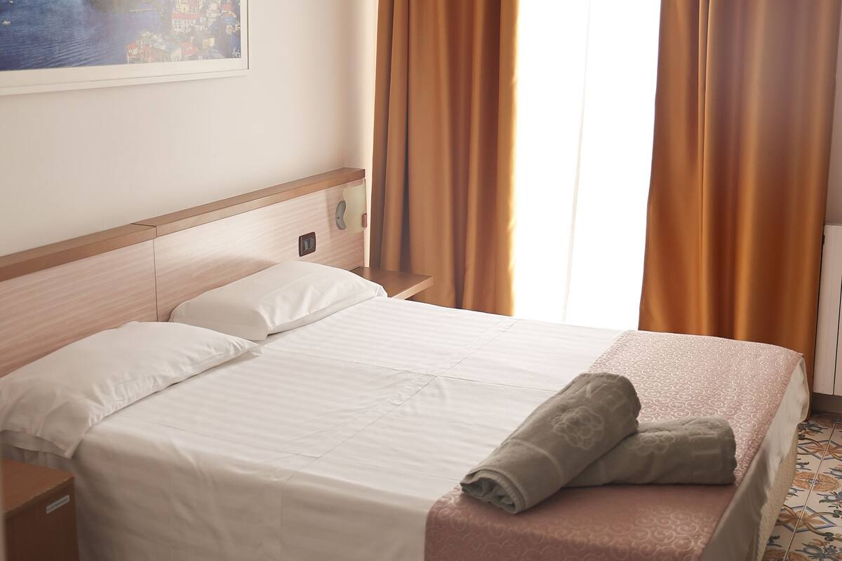 Une chambre d’hôtel avec un lit, une table de chevet, un tableau représentant un paysage côtier et des carreaux de sol à motifs.