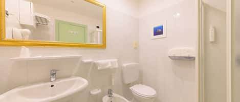 A bathroom with a sink, bidet, toilet, and a shower.
