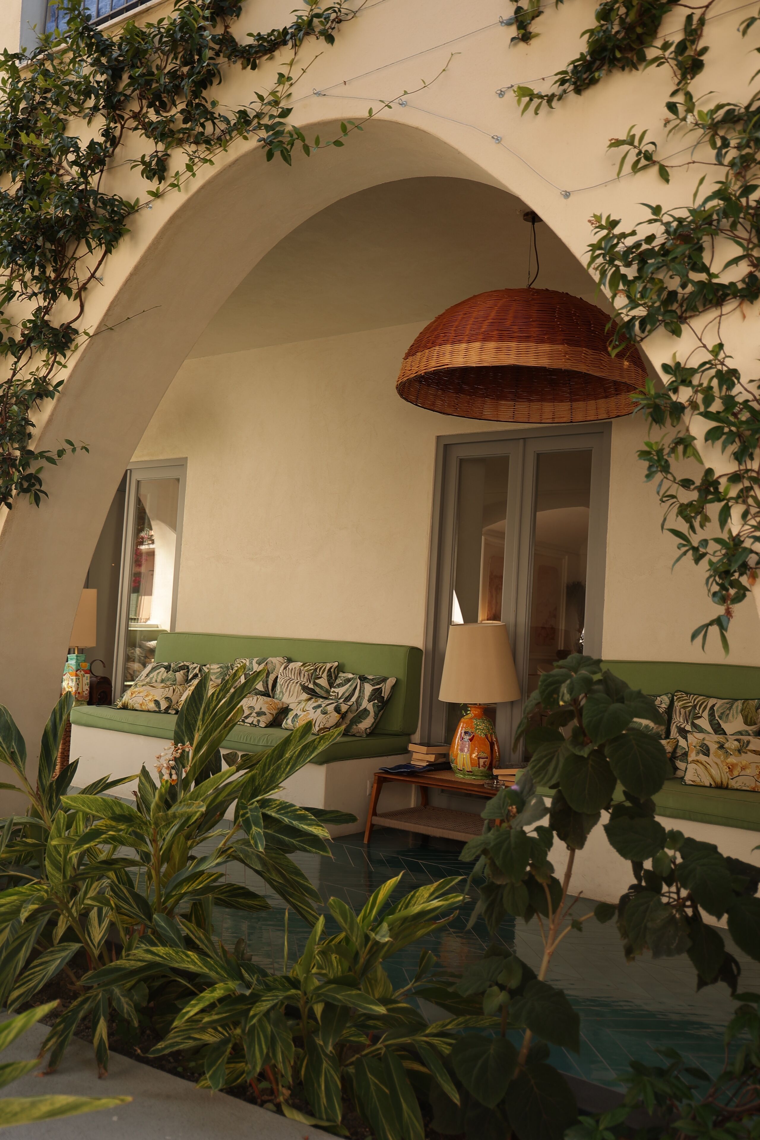 A cozy room with a green sofa, a wicker lamp, and a window with a view.