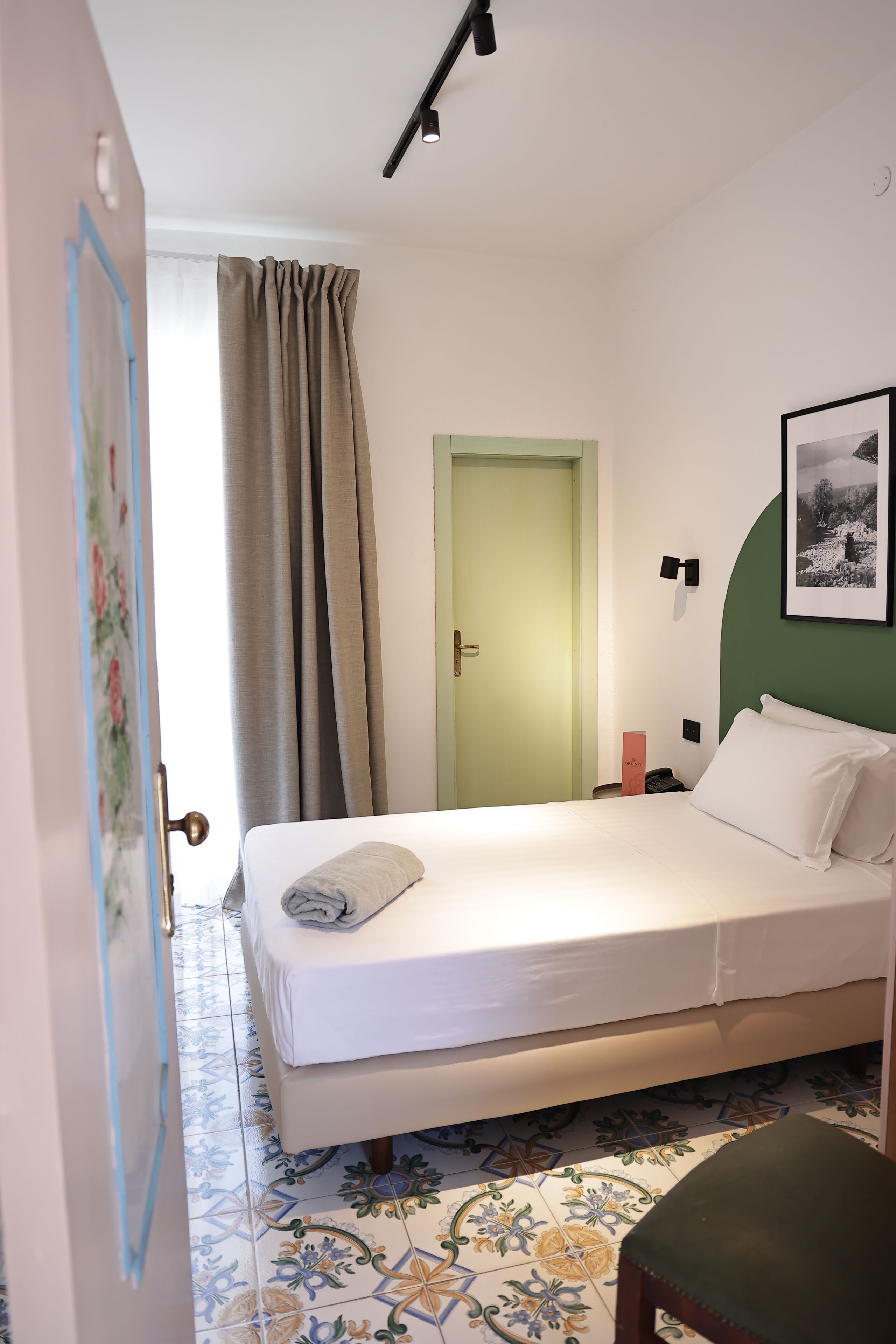 A neatly arranged bedroom with a bed, a chair, a door, and a wall-mounted light fixture.