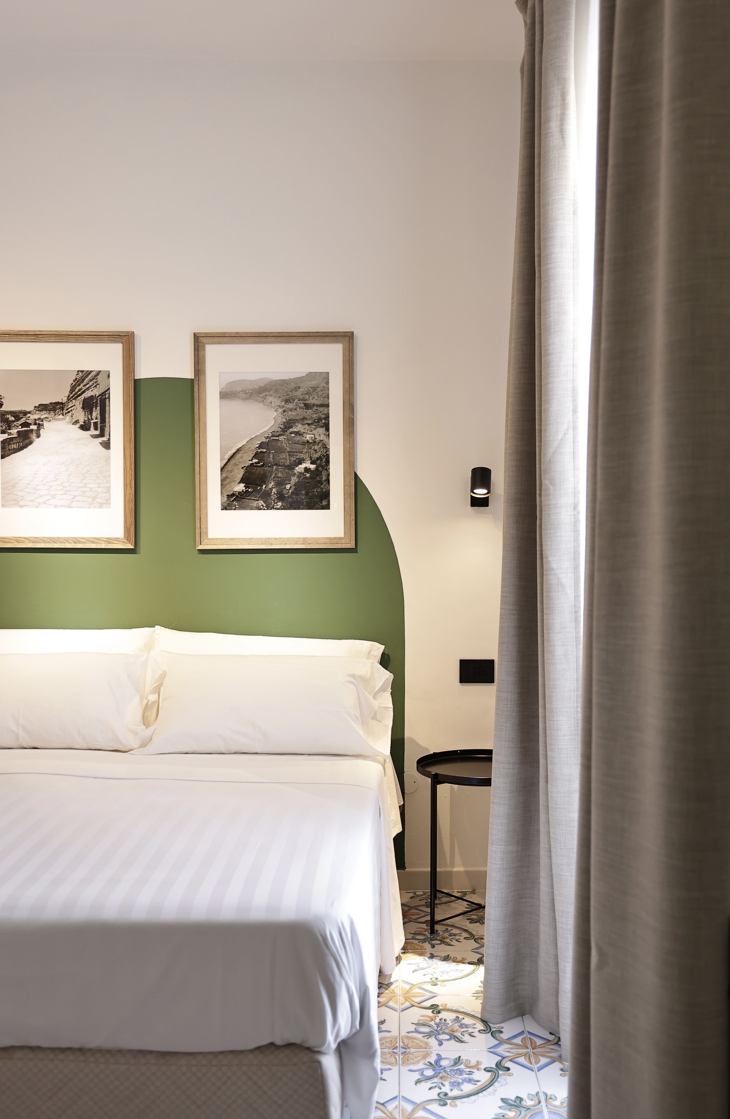 Una camera d'albergo con un letto, due quadri appesi al muro, un tavolino e una tenda.