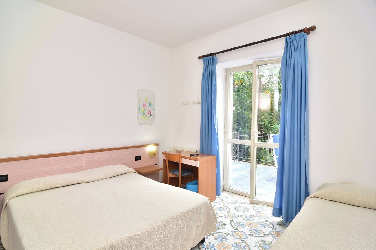 Une chambre d’hôtel avec deux lits, un bureau et une fenêtre avec des rideaux bleus.