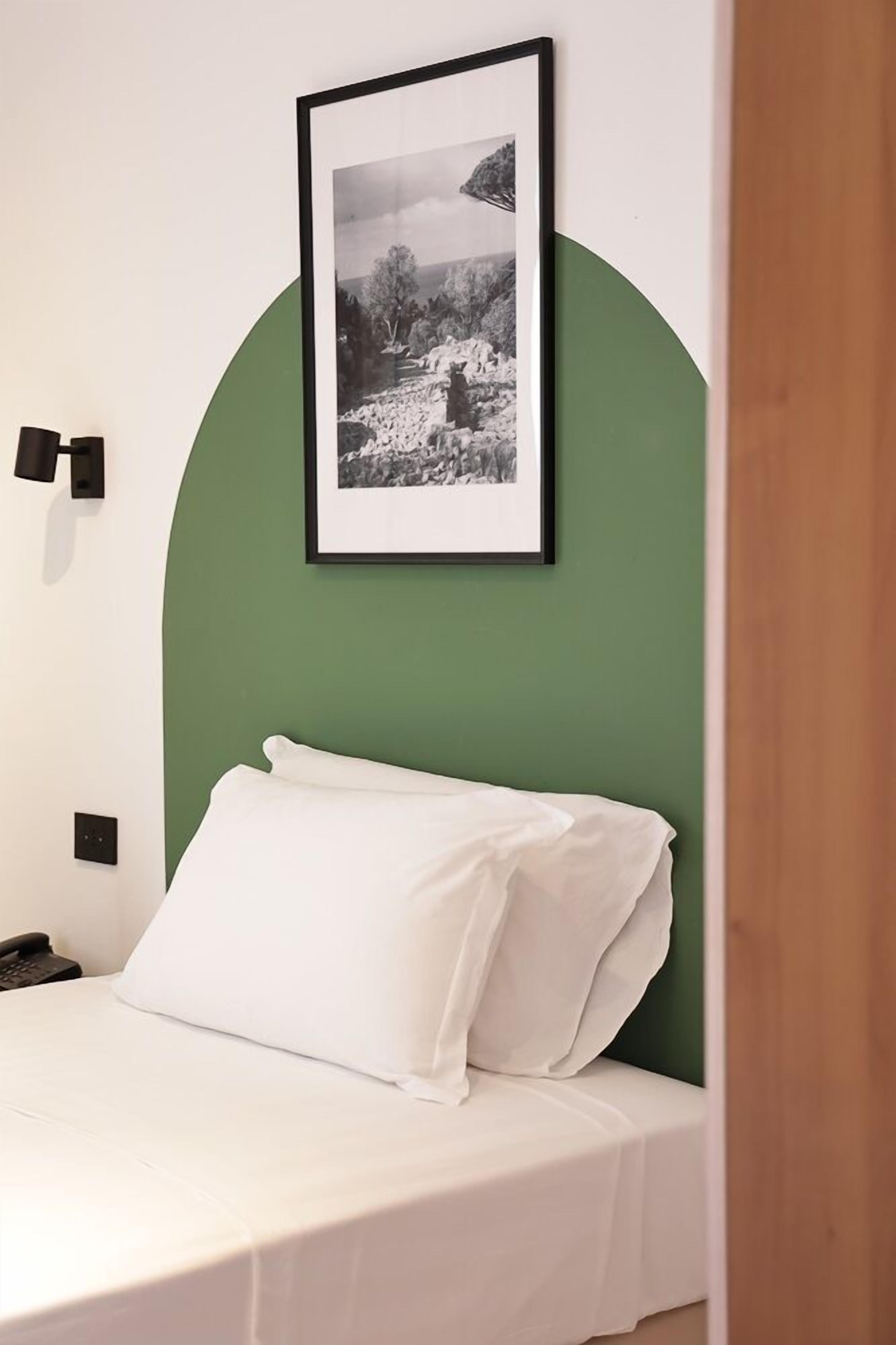 Un lit bien fait, avec du linge de lit blanc, une photographie en noir et blanc encadrée accrochée au mur, et un mur d’accent de couleur verte.