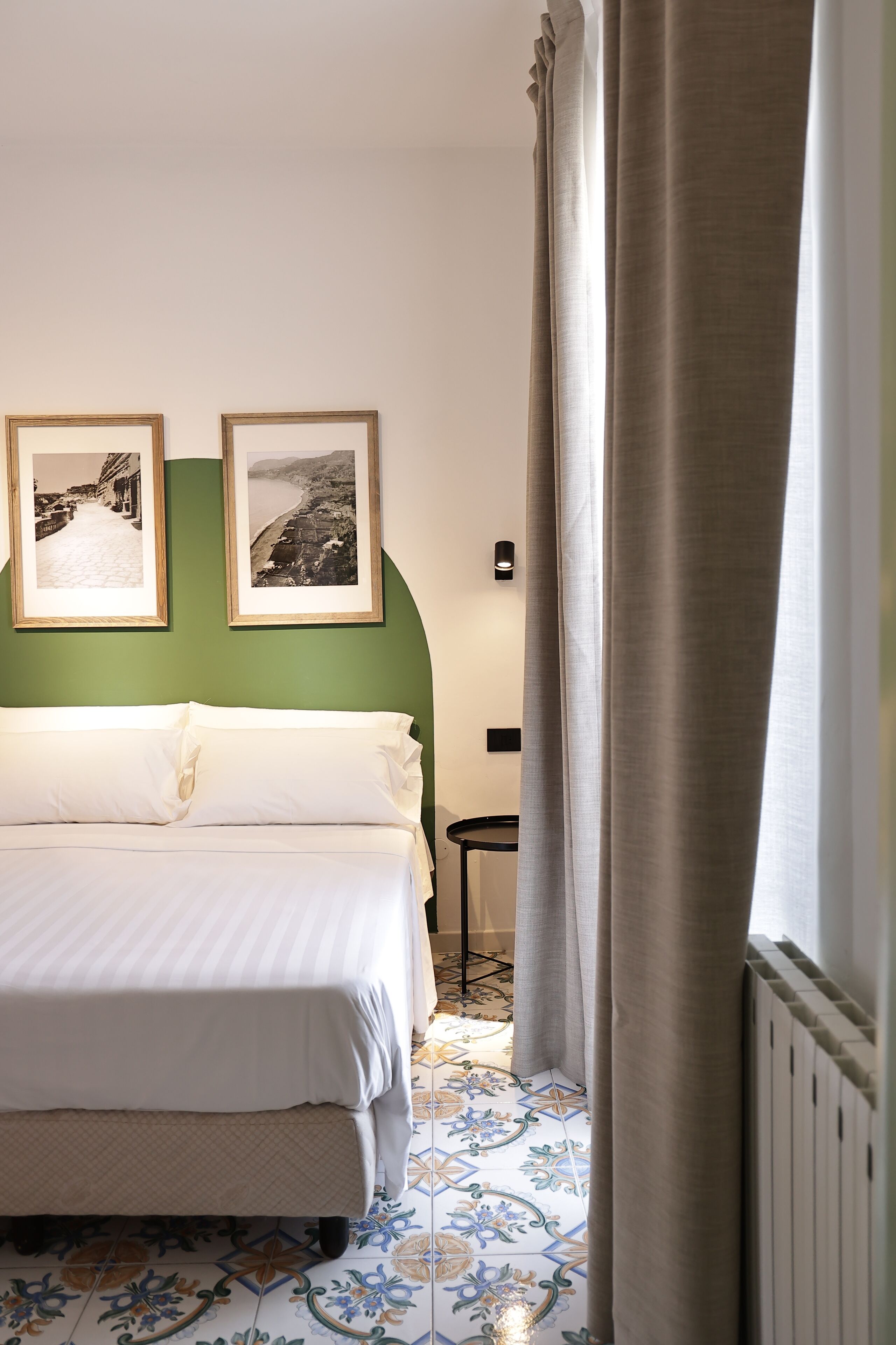 Una cama bien hecha con sábanas blancas, una pared verde decorativa y dos cuadros enmarcados.