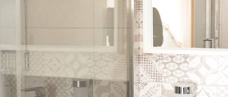 A modern bathroom with a glass shower enclosure, a white sink, and patterned tiles.