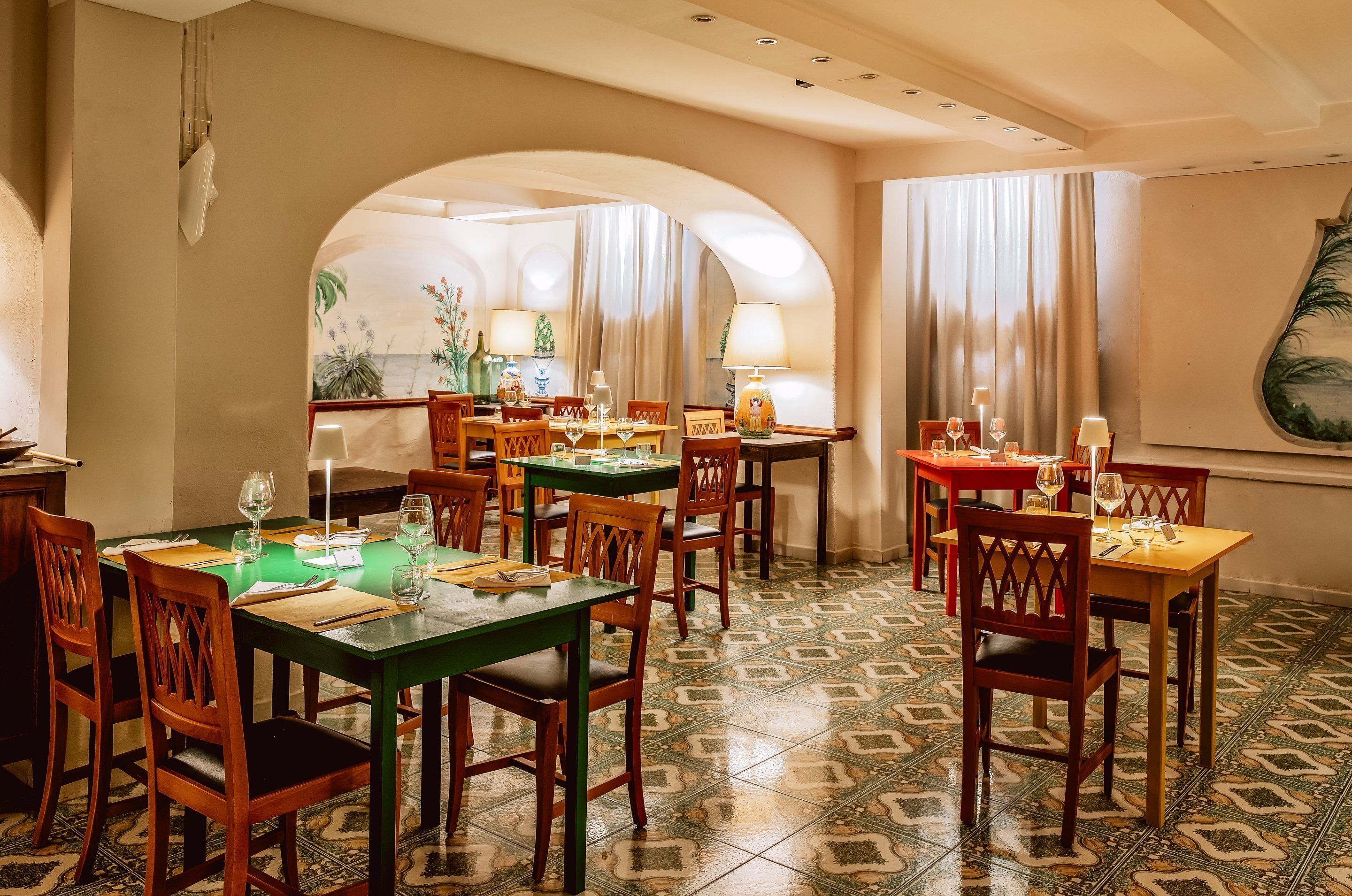 A restaurant with multiple tables and chairs, featuring a tiled floor and arched ceiling.