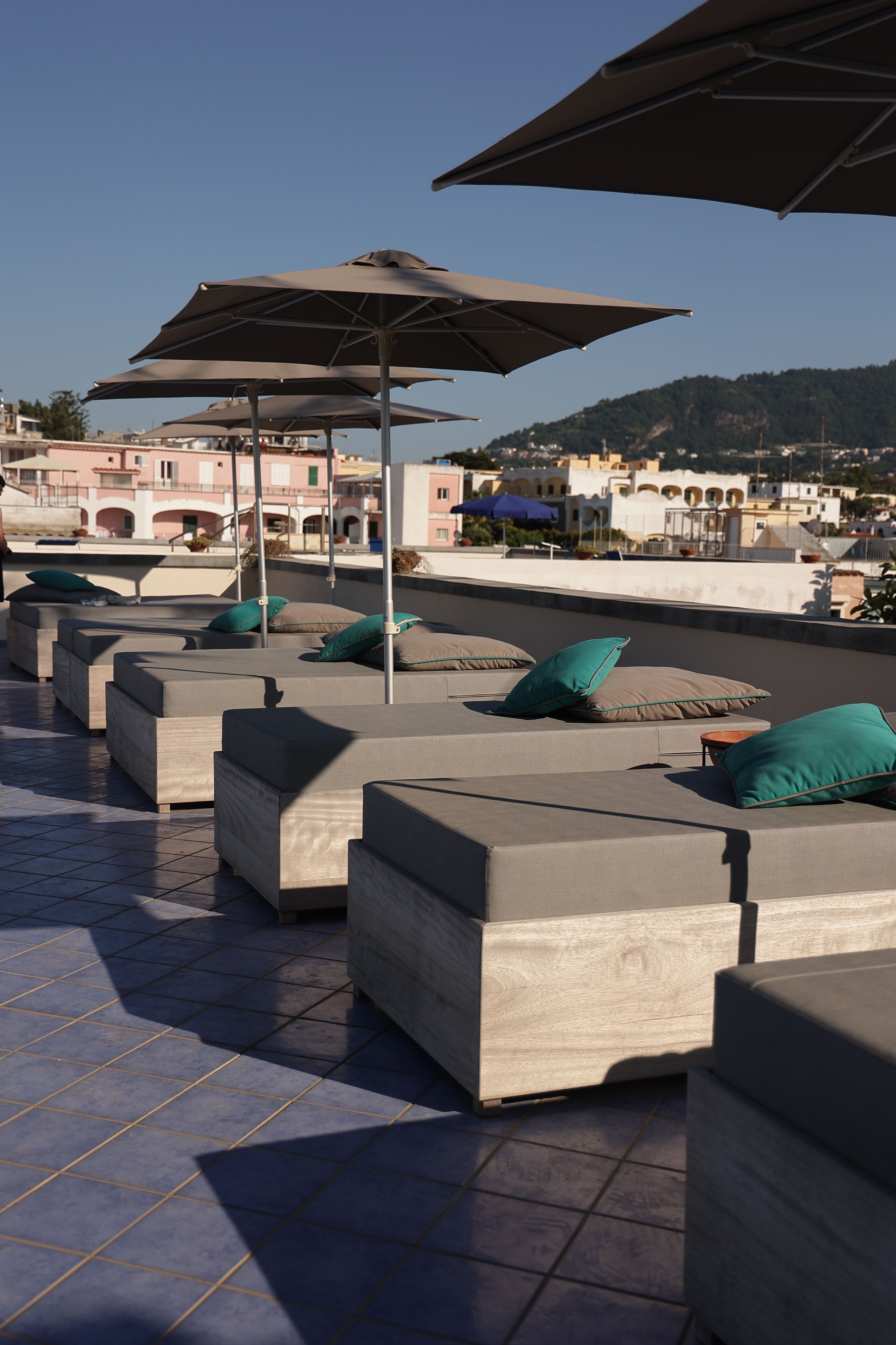 Outdoor seating with umbrellas, a tiled floor, and a view of buildings in the background.