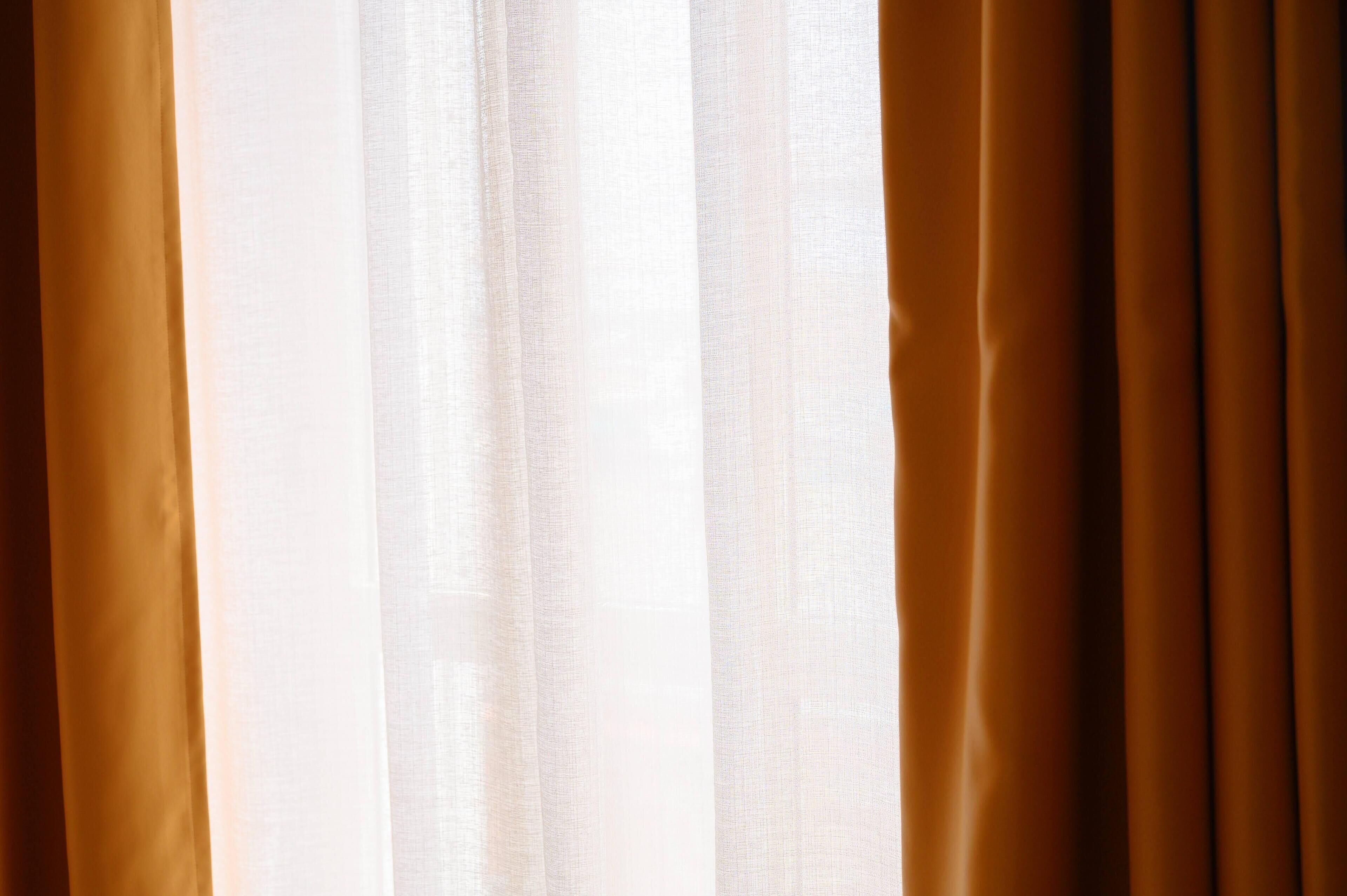 A view of a window with sheer white curtains and solid brown curtains.
