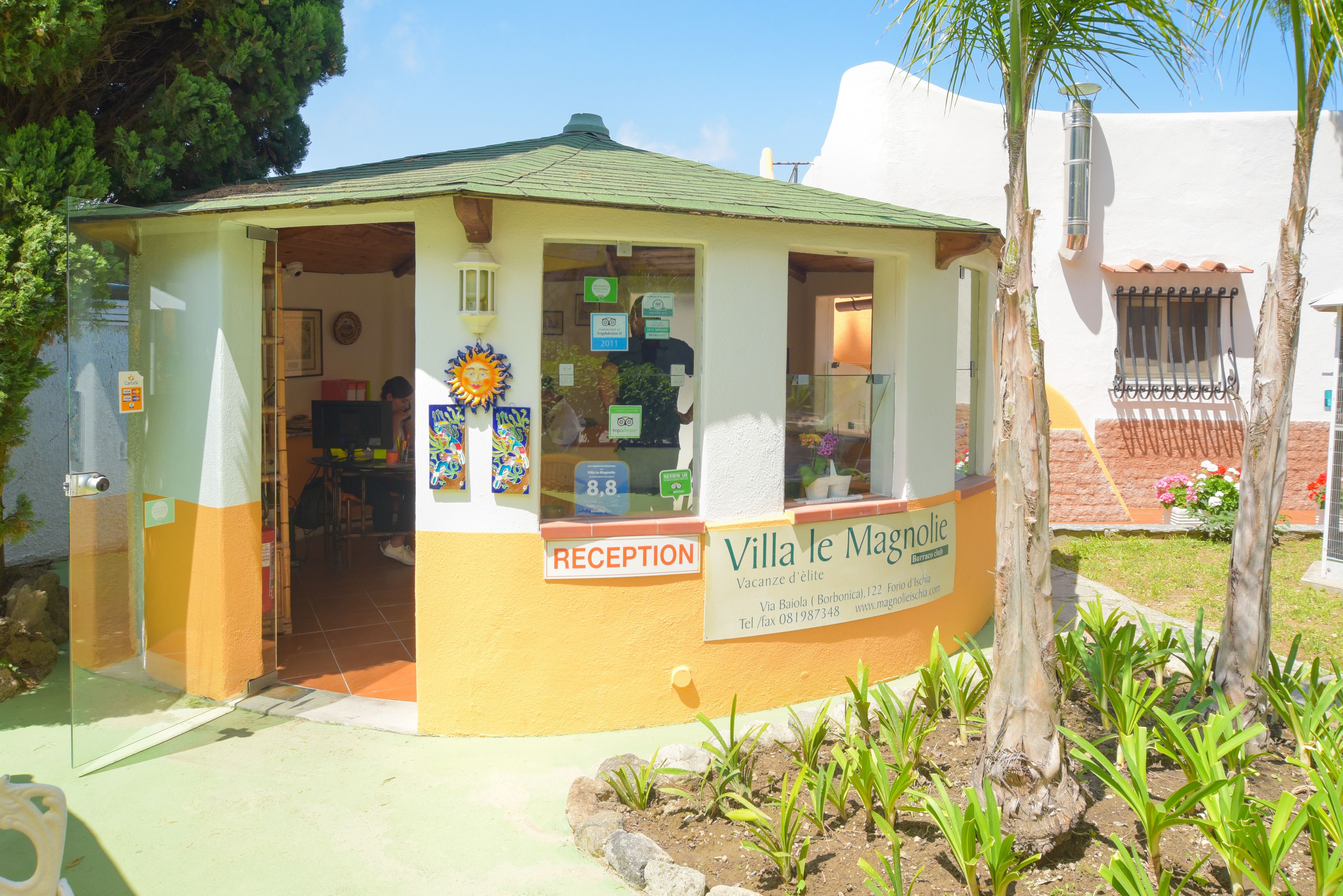 A reception area with a sign for Villa le Magnolie, including a reception desk and a window with a view of the interior.