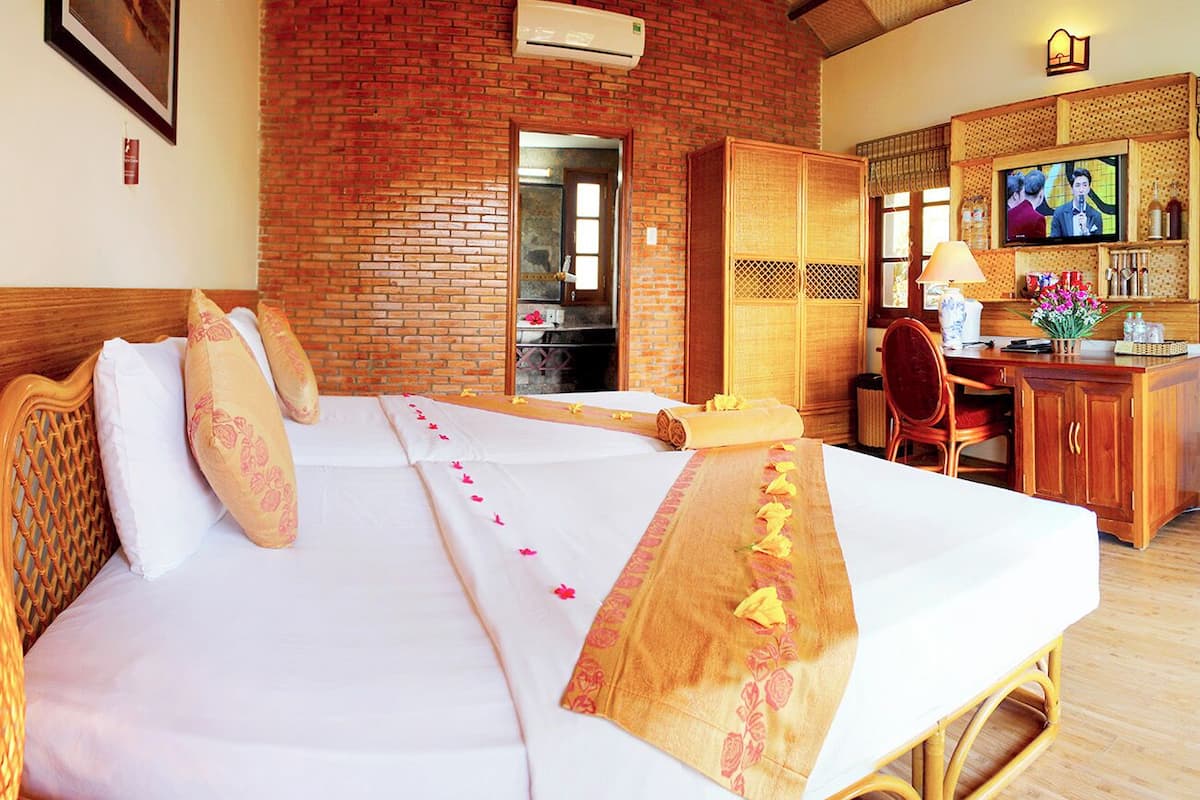 A hotel room with a large bed, a wooden desk, a television, and a brick wall.