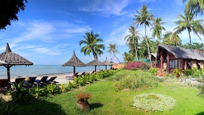 Un complexe hôtelier tropical doté de bâtiments à toits de chaume, offrant une vue sur la plage et entouré d’une végétation luxuriante.
