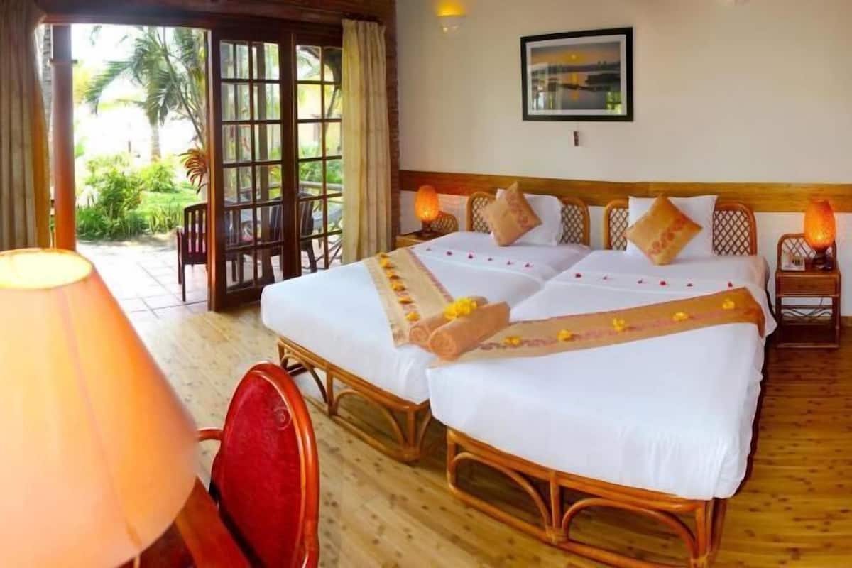 A hotel room with two beds, a wooden floor, a window with a view, and a lamp.