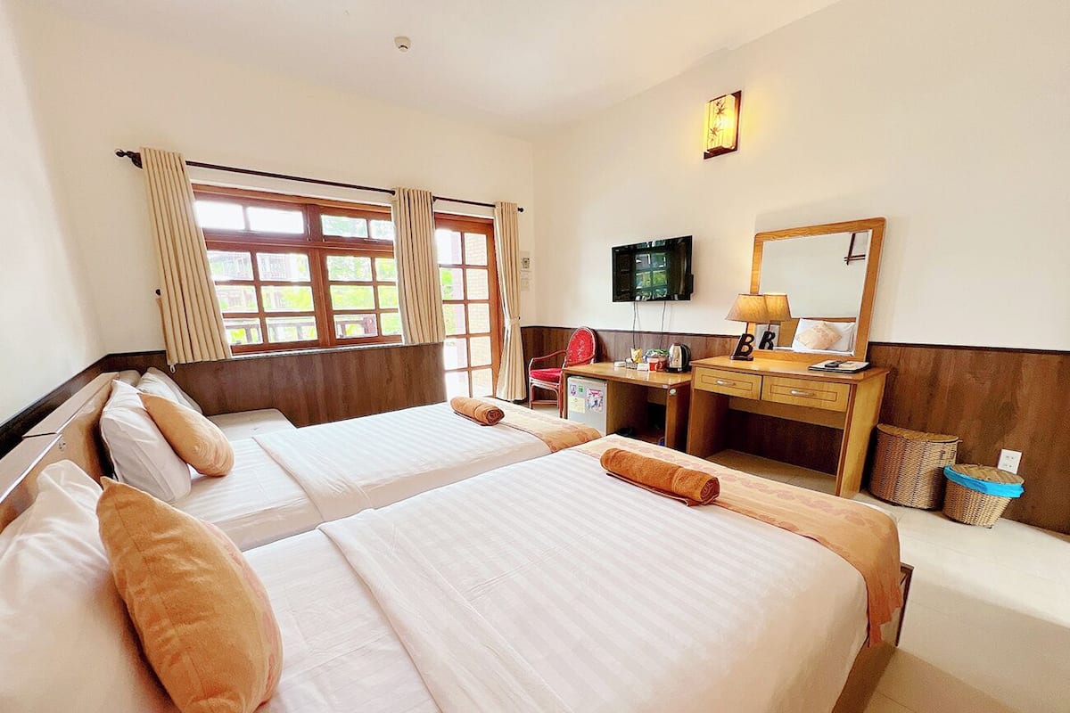 A hotel room with two beds, a desk, a TV, and a window with curtains.