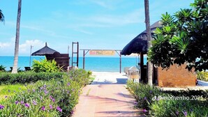 Un sentier menant à une zone de plage bordée de palmiers, où se trouve un panneau indiquant « Lant Munac Cottages ».
