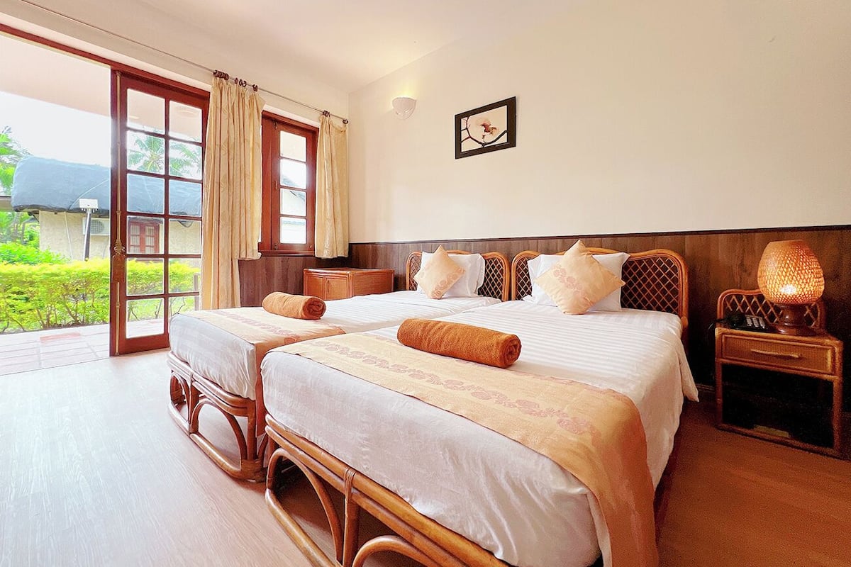 A hotel room with two beds, a large sliding glass door, and a bedside table with a lamp.