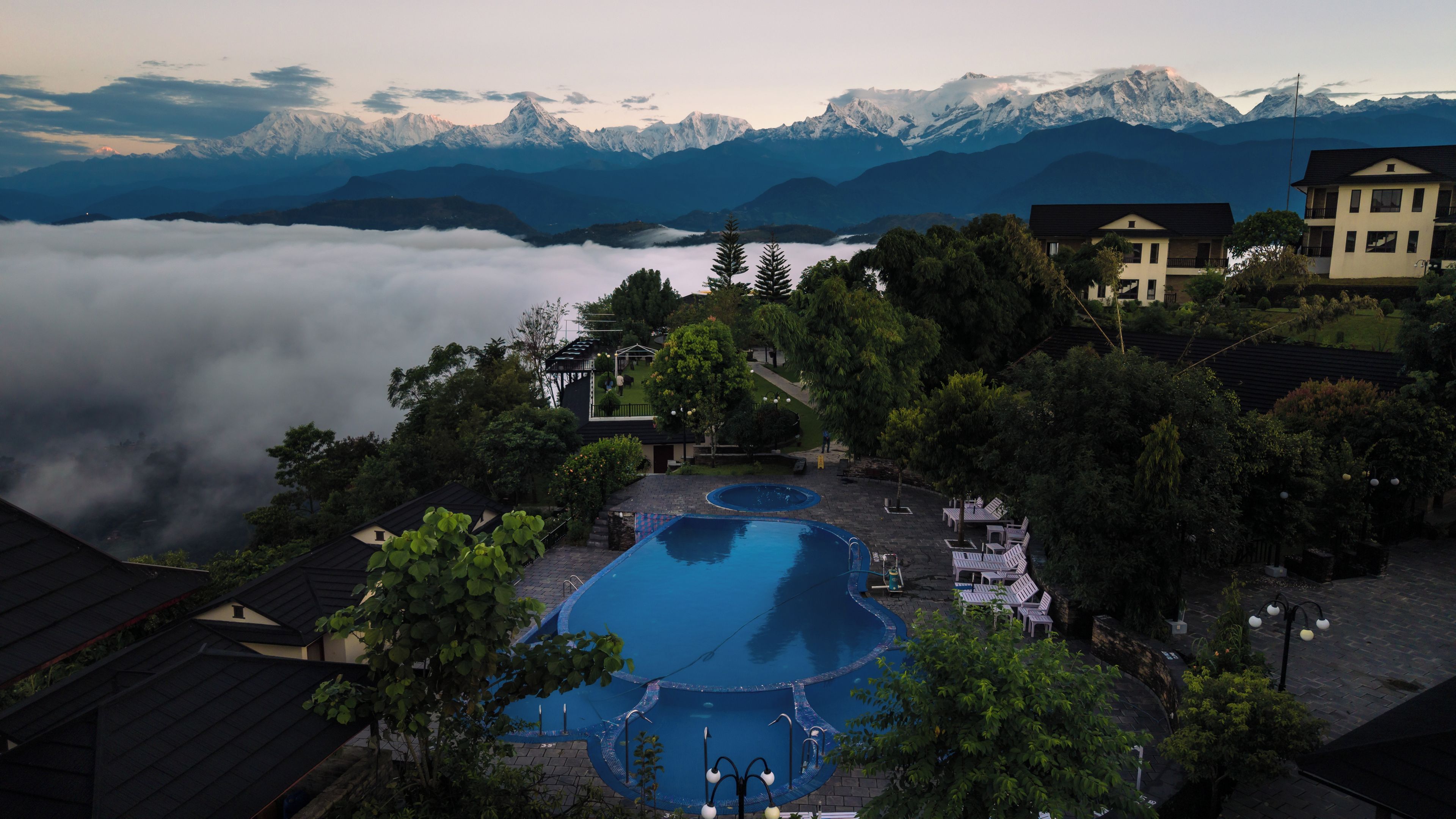 A resort with a swimming pool, surrounded by trees and mountains in the background.