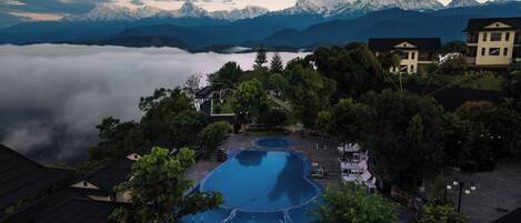 A resort with a swimming pool, surrounded by trees and mountains in the background.