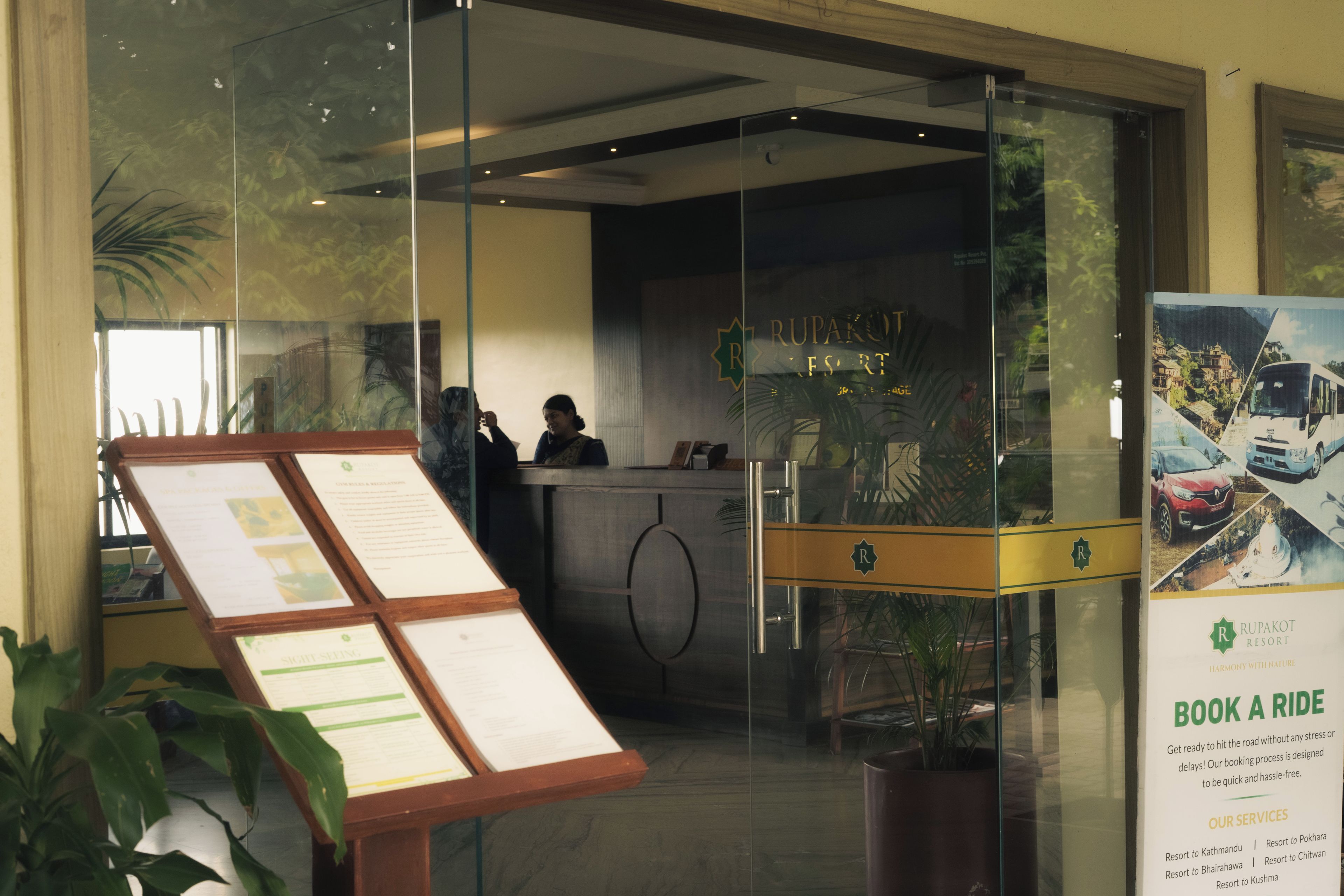 A reception desk with a glass partition, a signboard with text, and a poster advertising a ride service.